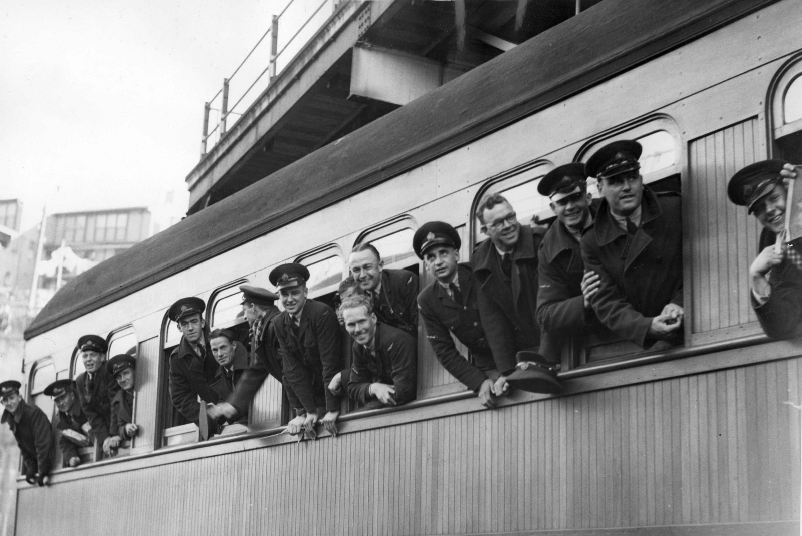 Black and white photograph of service men in unform hanging out of the windows of a train car