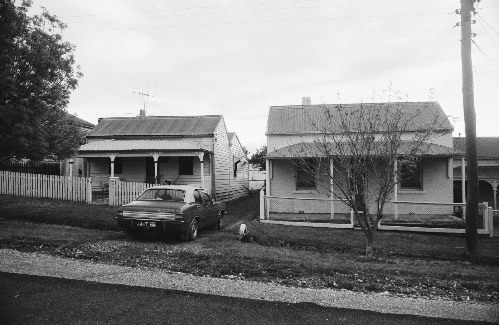 Black and white phrotograph of front views of single story houses with a car parked in front