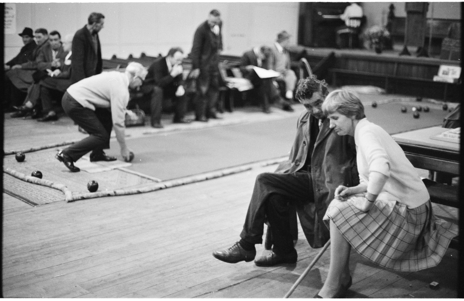 Black and white photograph of men and women sitting watching a game of indoor bowls