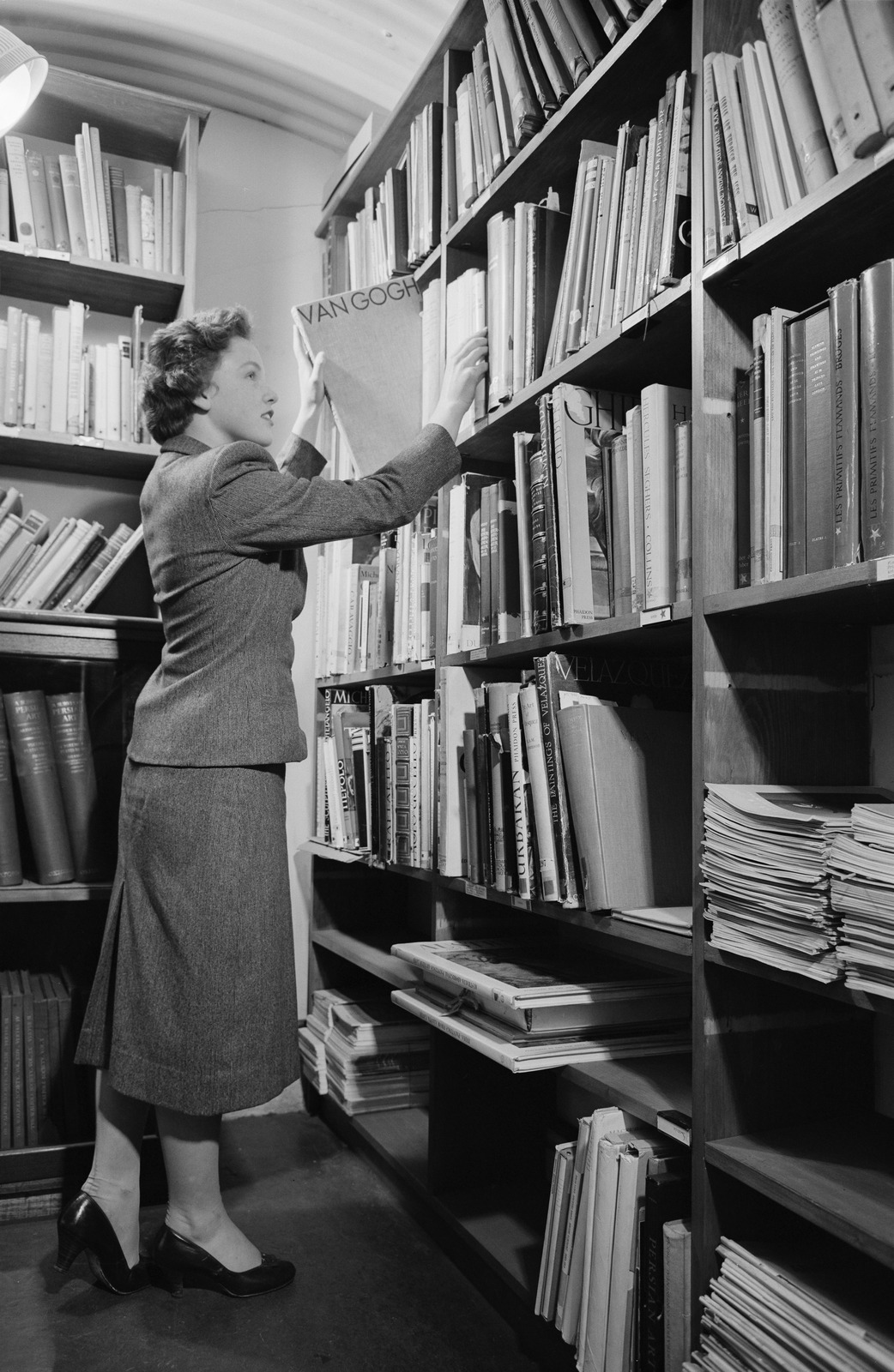 Black and white photograph of a women placing an item onto a library shelf full of books