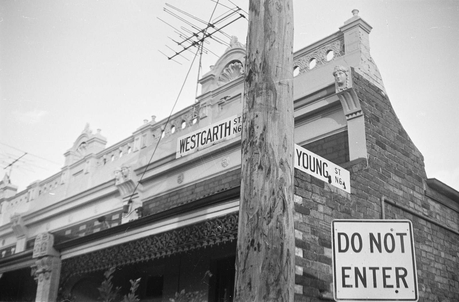 Black and white photograph showing street signs on pole: Young St. and Westgarth St.; laneway and Do Not Enter sign; single storey brick cottages