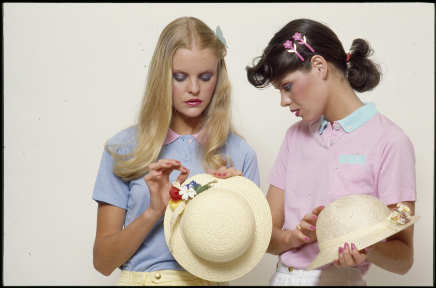 Two young women modelling casual wear in pastel colours, both holding hats