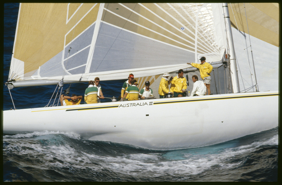 Side view of  Alan Bond's America's Cup 12 metre yacht Australia III under sail, with sailors on deck