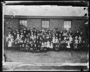 Group portrait of school children in front of brick building