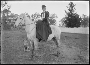 Portrait of woman seated side-saddle on horse, dog sitting beside them