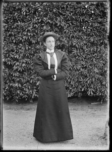 Portrait of woman standing, arms folded, in front of garden hedge