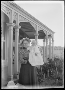 Portrait of woman in sunhat holding infant, outside house