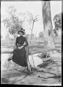 Portrait of woman in black dress sitting on a log in bushland