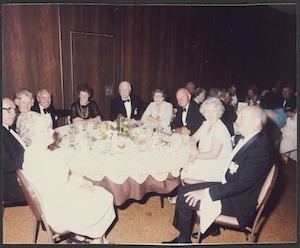 Group of men and women sitting round dining table at retirement dinner for Lance R. Robinson